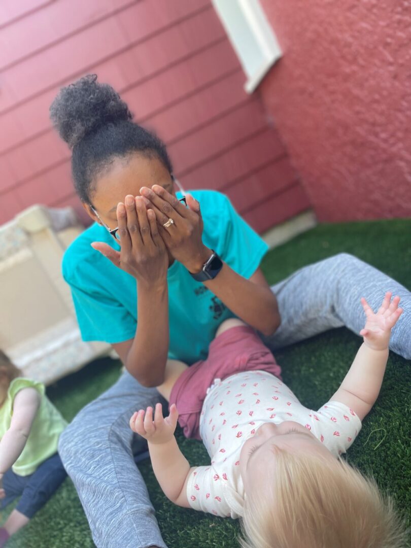 A woman sitting outside with a baby lying on the ground.