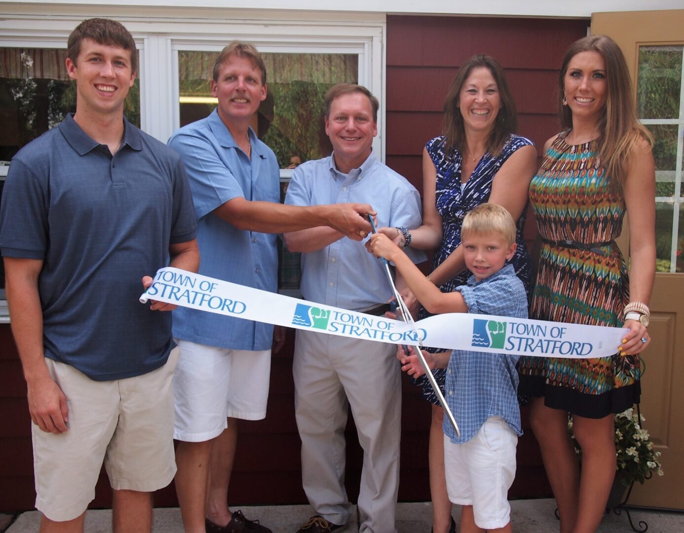 Family and friends celebrate a ribbon-cutting event outdoors.