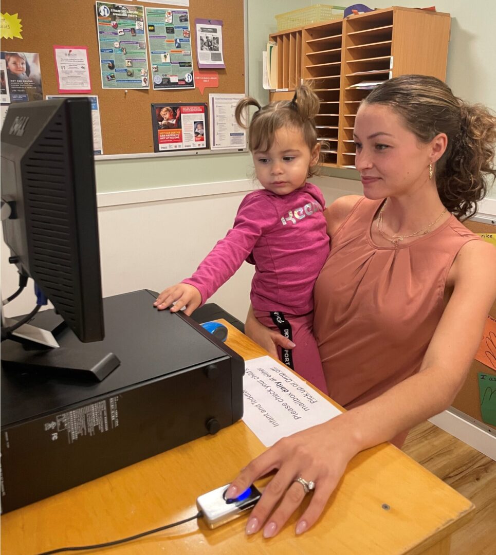 A woman and a young girl smiling and using a computer together.